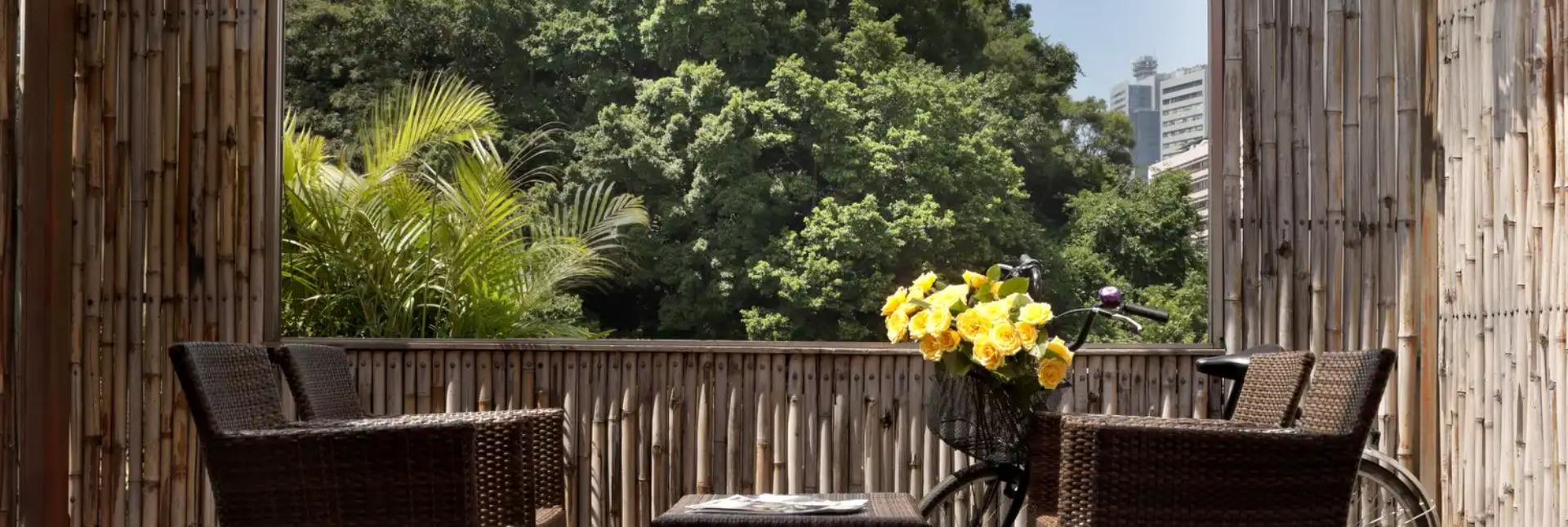 Tropical balcony with wicker chairs, flowers, and distant city skyline.